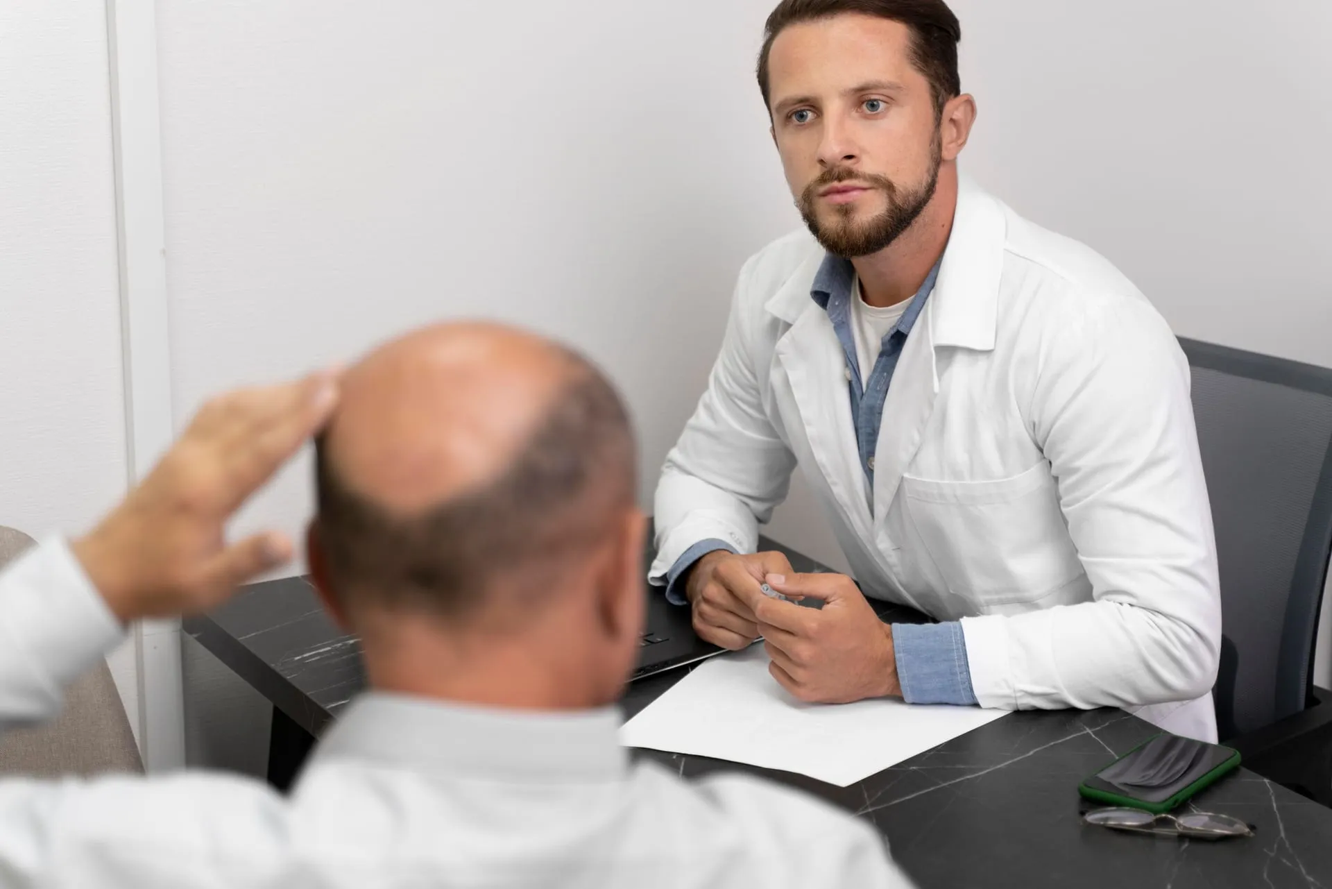 Doctor talking to a patient who is touching the thinning back of his head